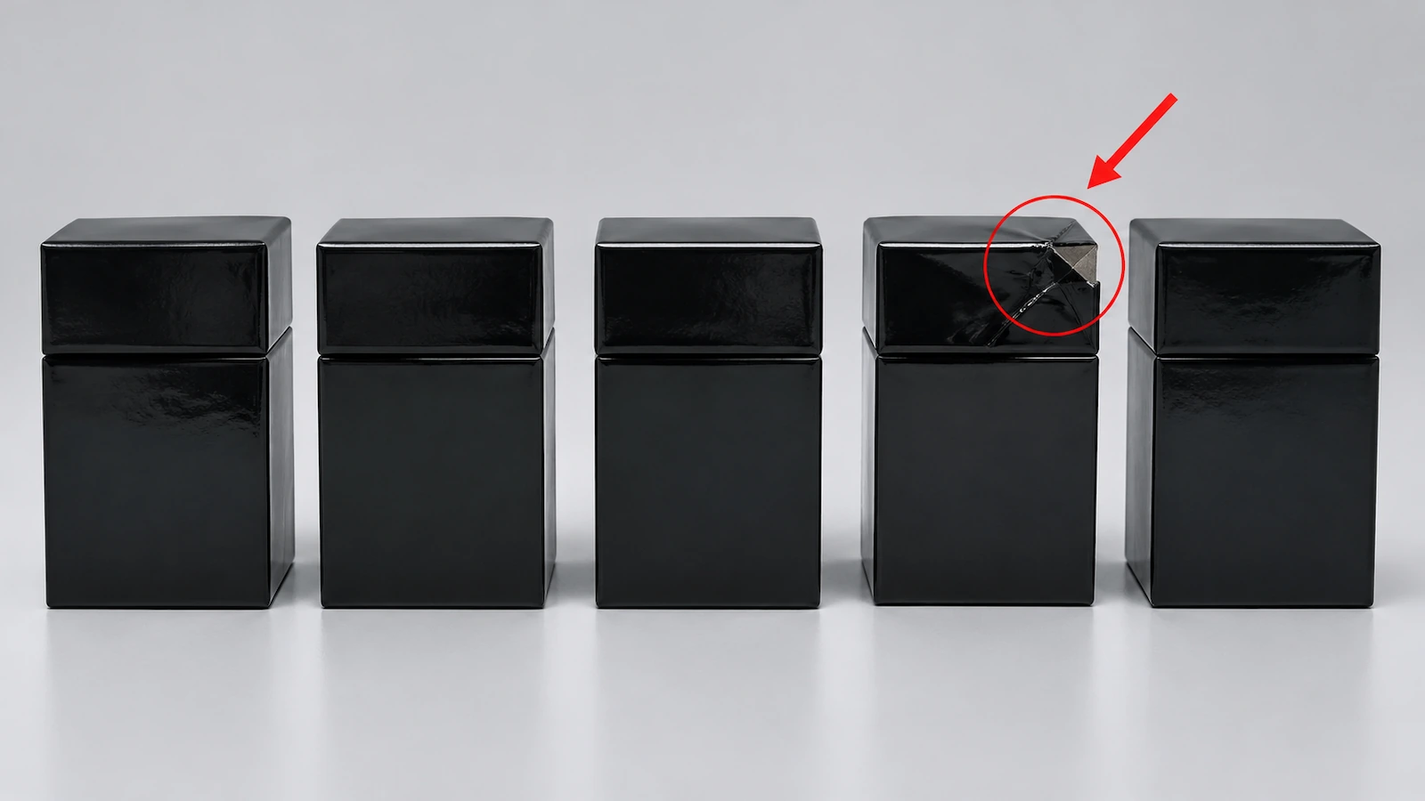 Fila de cajas rígidas negras idénticas de 2 piezas en la que una caja tiene una esquina aplastada resaltada con un círculo rojo y una flecha diagonal roja