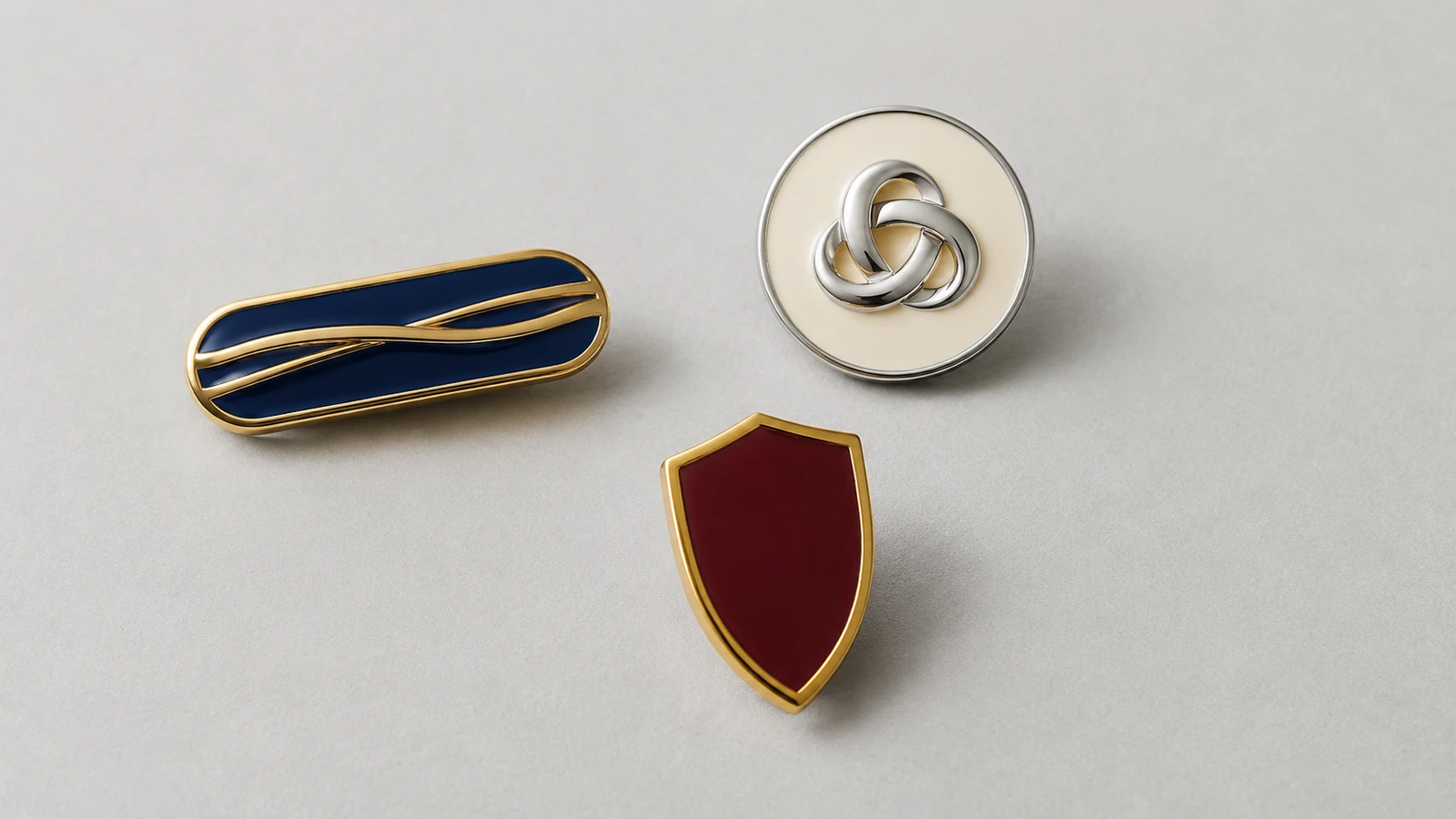 Pins minimalistas sin diseño con cintas de metal en relieve lisas y una forma de lazo entrelazado que sugieren tipografía sin ningún carácter legible