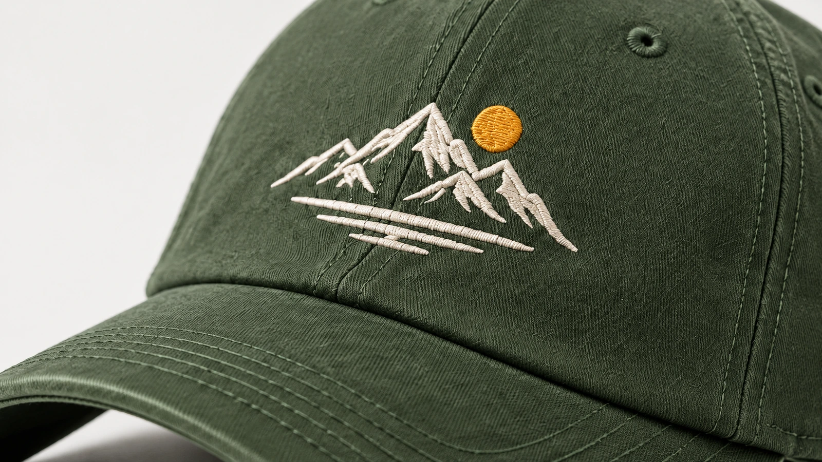 Primer plano del bordado de montaña blanca y un sol amarillo sobre una gorra verde