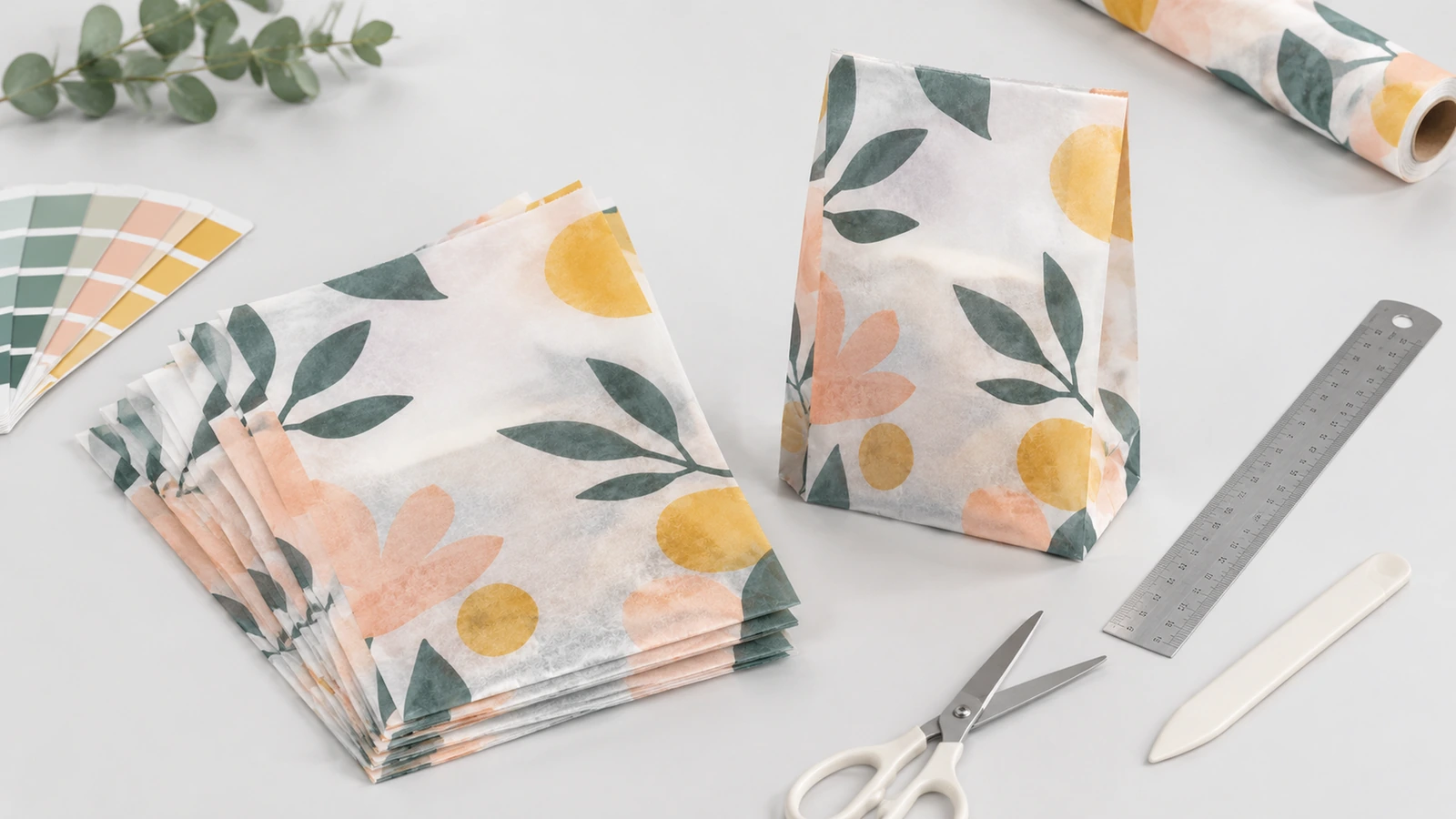 Bolsas de papel con estampado floral y materiales para hacer muestras Bolsas de papel translúcido estampadas con motivos florales, junto a un rollo de papel, una regla, tijeras y muestras de color