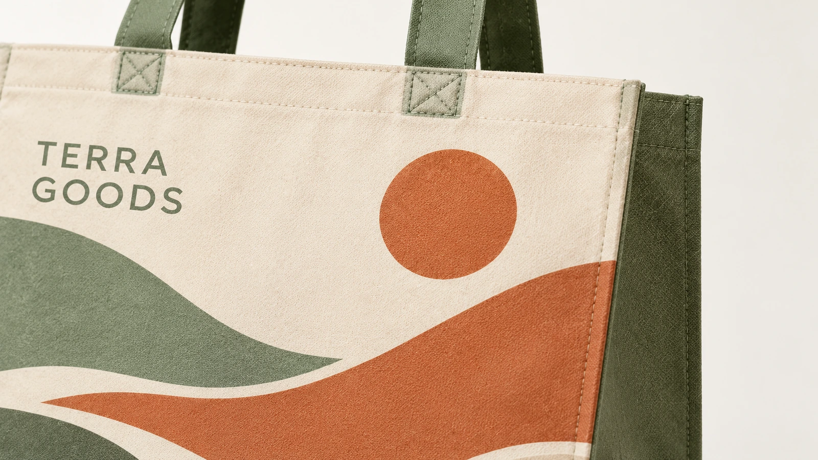 Primer plano de una bolsa tote con estampado de paisaje, con el texto TERRA GOODS y asas verdes cosidas