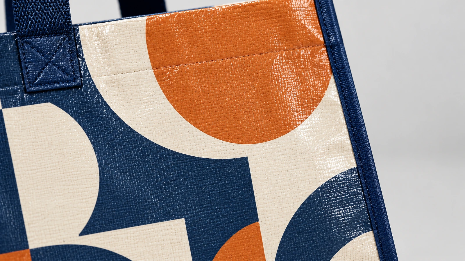 Superficie estampada y costura de las asas Primer plano de la tela tejida estampada con motivos geométricos y de la unión reforzada del asa azul marino