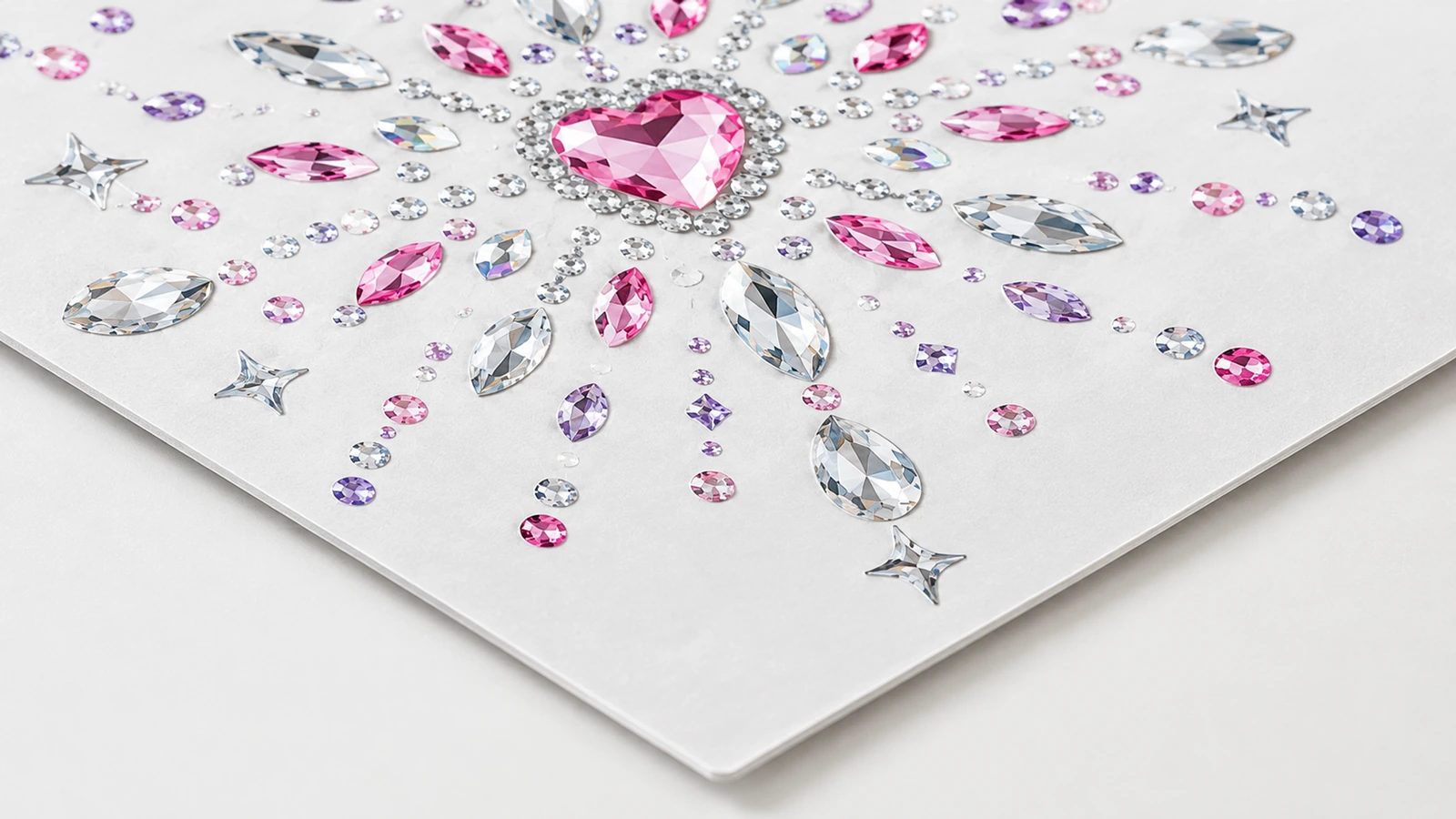 Primer plano de un motivo de strass Primer plano de un motivo de strass rosa con centro en forma de corazón y piedras transparentes, rosas y moradas sobre una hoja blanca