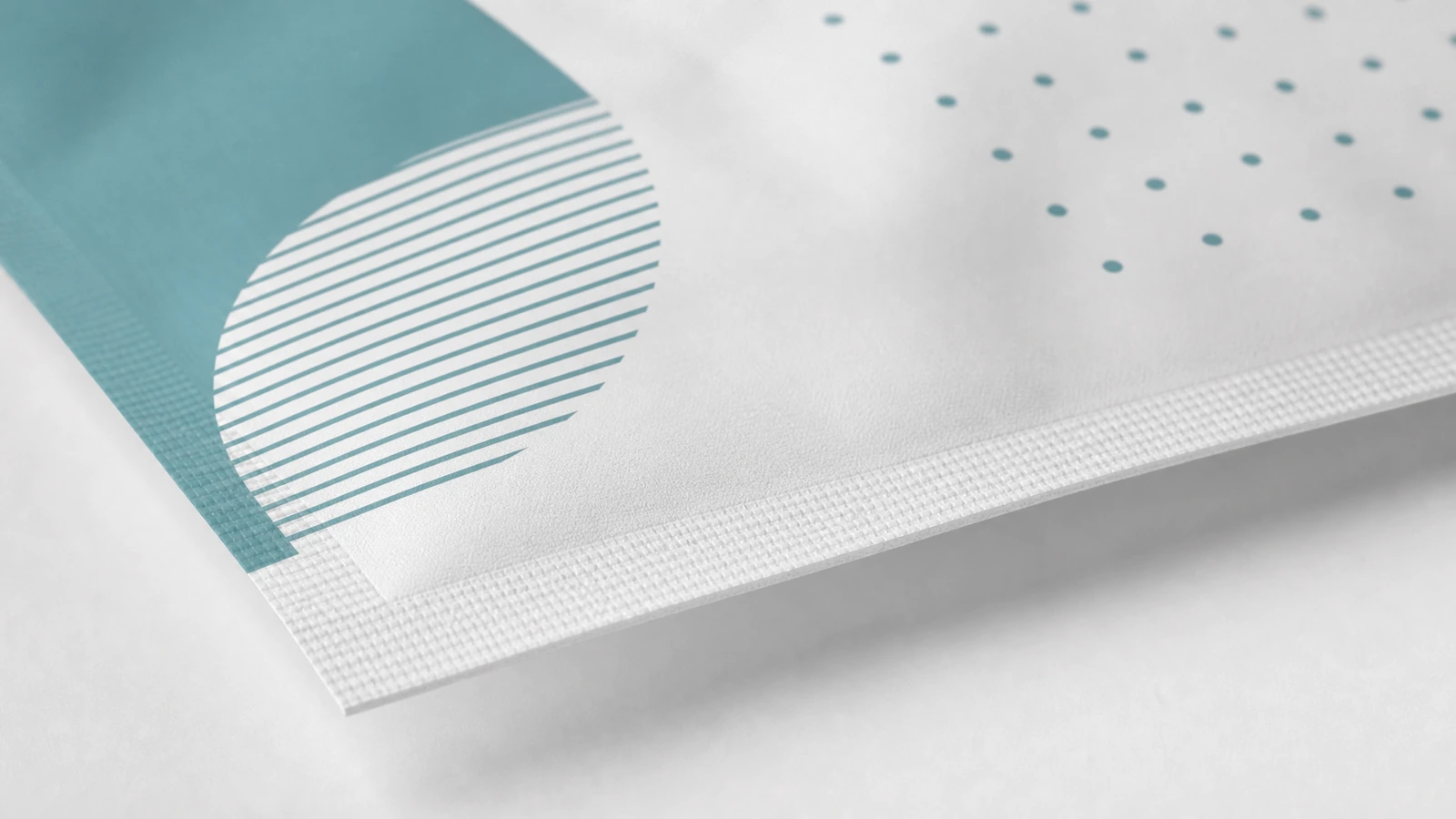 Detalle del estampado y del borde sellado de la bolsa Primer plano del estampado geométrico verde azulado y del borde sellado texturizado de una bolsa blanca